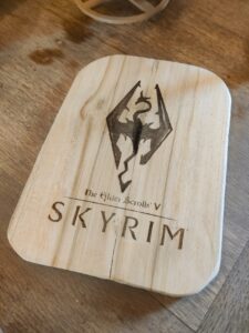 Wooden cutting board engraved with The Elder Scrolls V: Skyrim logo and dragon emblem on a light wood surface.