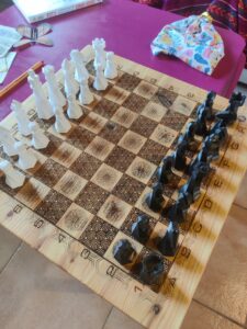 White and black chess pieces arranged on a decorative wooden chessboard, ready for a game on a pink table.