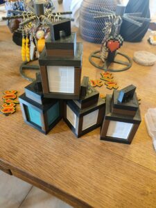 Three black 3D-printed mini houses with white window panels sit on a wooden table, brown trim and layered roofs visible.