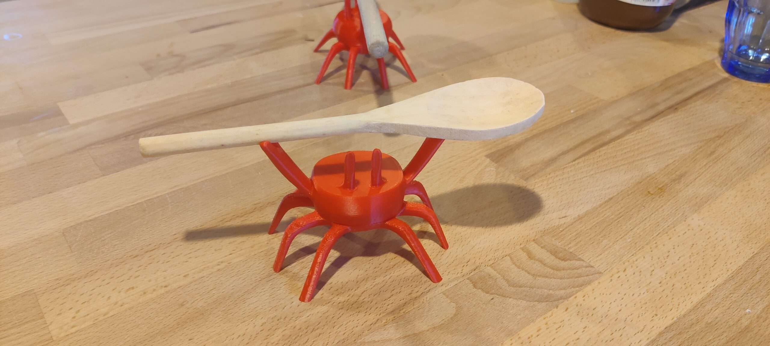 Crabe porte-cuillère en PLA – vue de face ‣ Atelier 34 Vue de face du crabe en PLA soutenant une cuillère en bois
