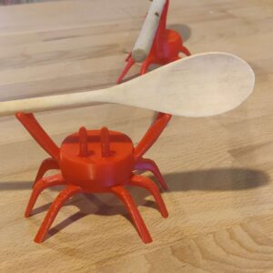 Crabe rouge orangé imprimé en PLA tenant une cuillère en bois sur ses pinces