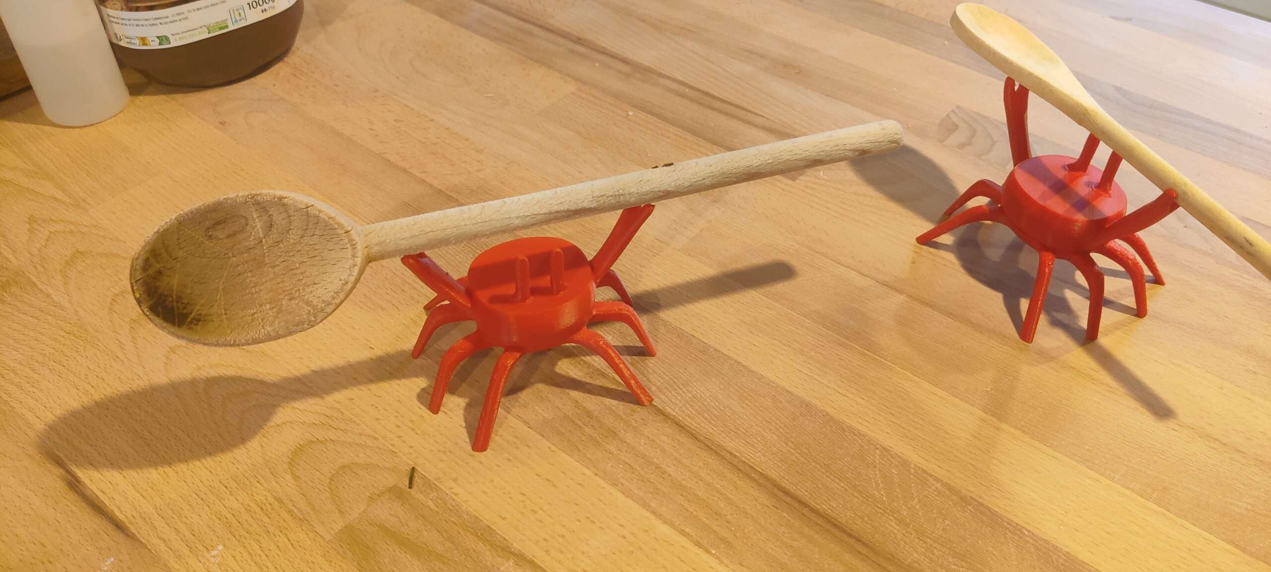 Crabes porte-cuillère en PLA – exemples d’utilisation ‣ Atelier 34 Deux crabes rouge orangé servant de supports pour des ustensiles en bois