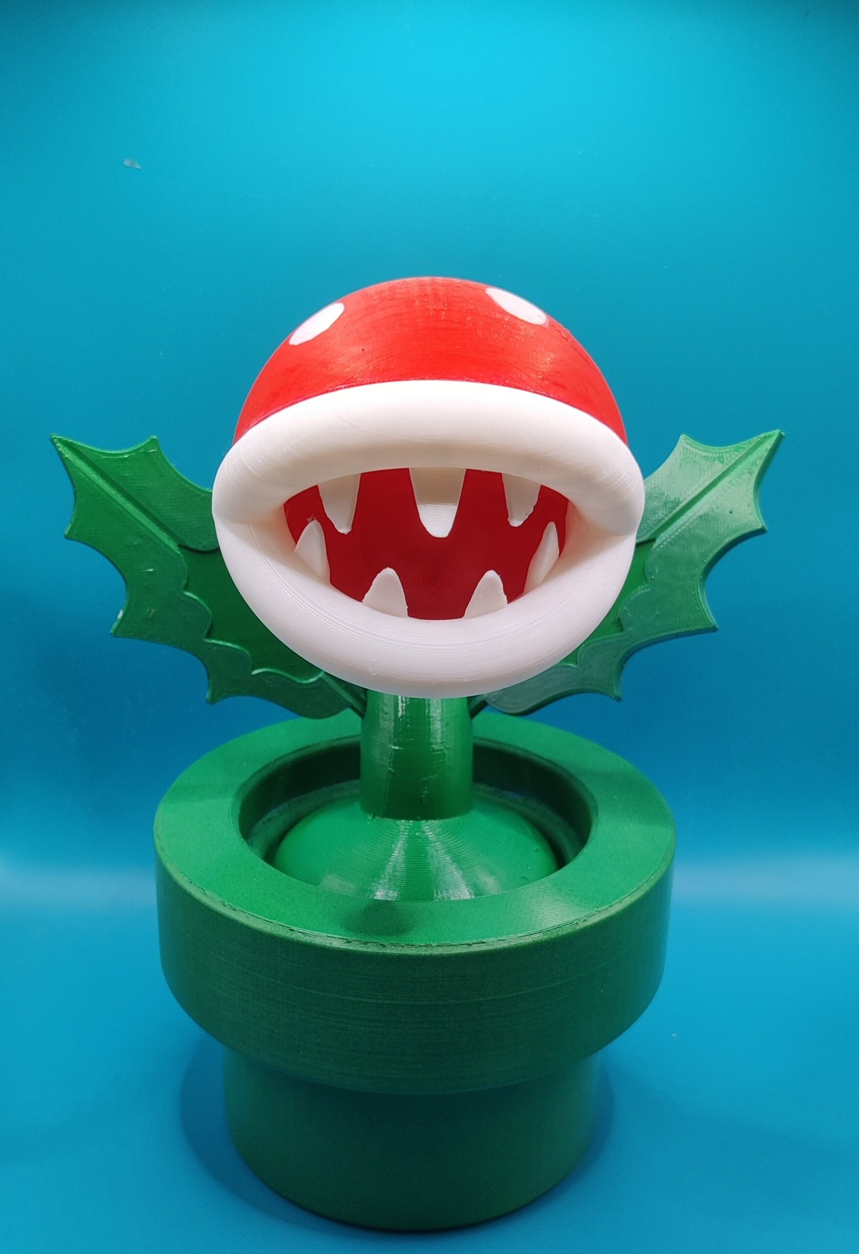 Plante Piranha Mario – Vue de face ‣ Atelier 34 Vue de face de la Plante Piranha, bouche ouverte, dents blanches et feuilles vertes.